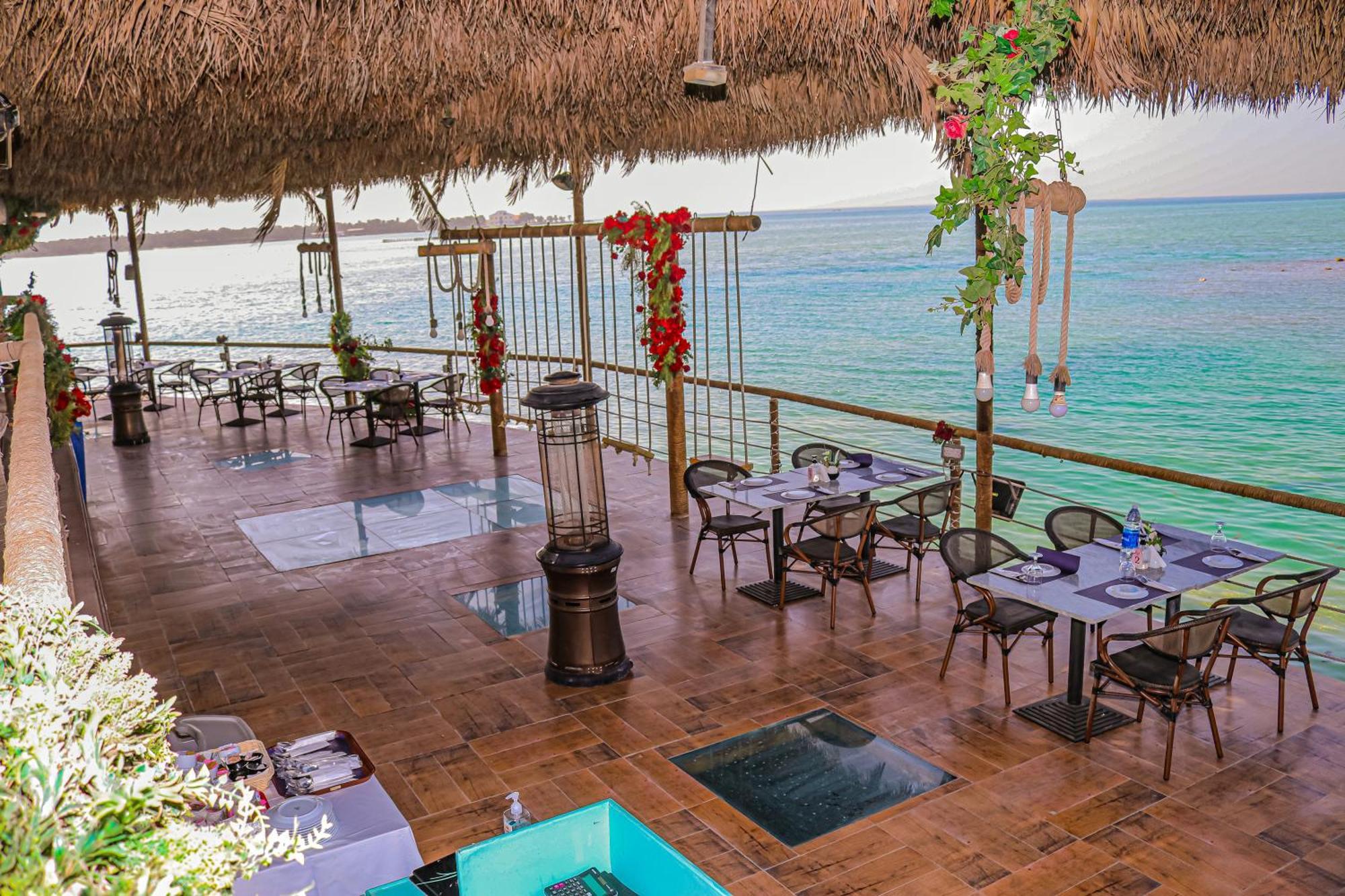 Lagoona Beach Luxury Resort And Spa Manáma Kültér fotó The photo depicts a coastal restaurant or dining area with an open-air design. It features a wooden floor and tables set for dining, surrounded by chairs. The space is partially covered by a thatched roof, providing shade while allowing for a view of