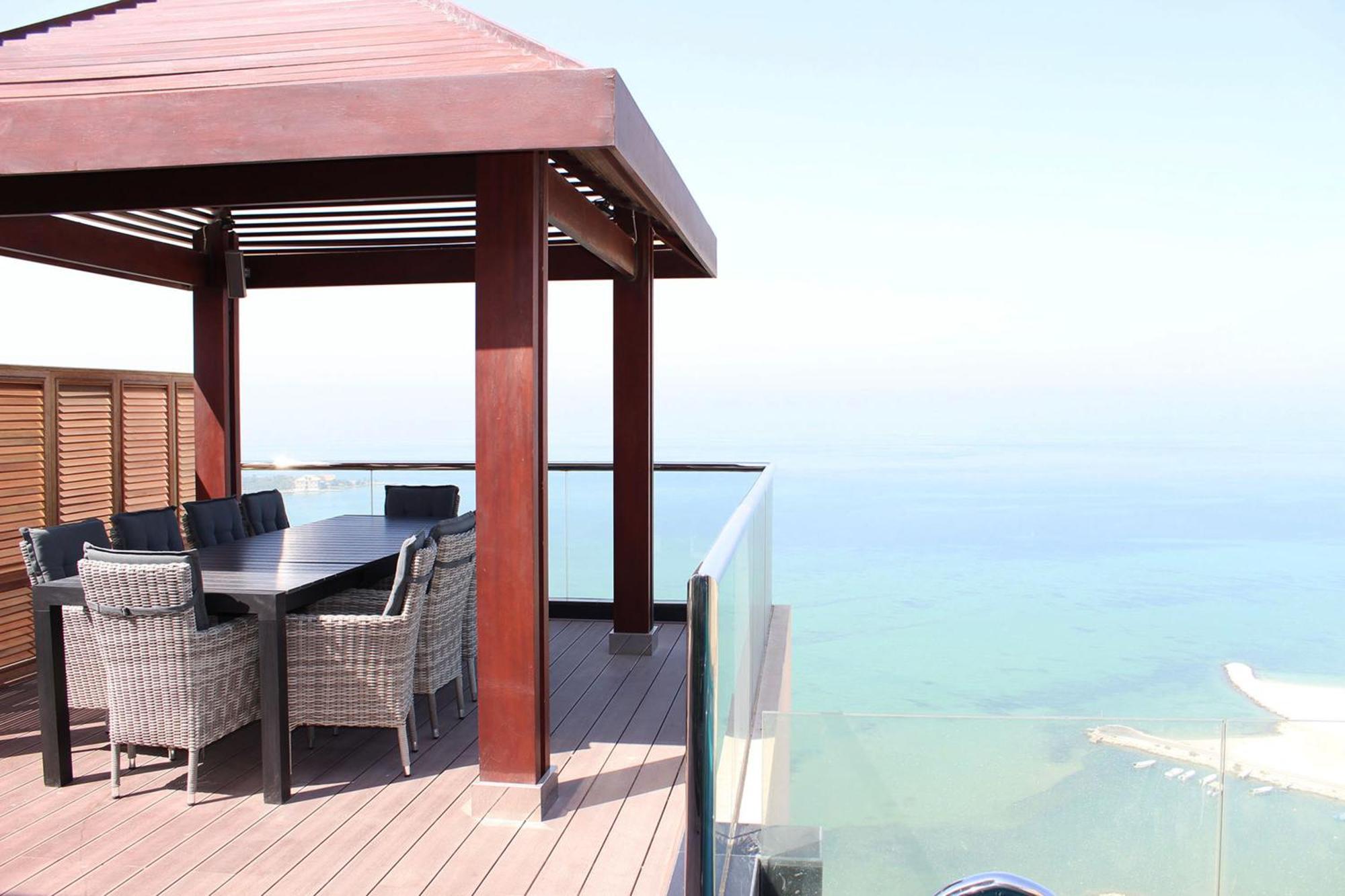 Lagoona Beach Luxury Resort And Spa Manáma Kültér fotó The photo showcases a stylish outdoor patio or terrace area. It features a wooden structure with a sloped roof, providing a shaded space. There is a large table made of dark wood, surrounded by several wicker chairs. The patio is elevated and has gla