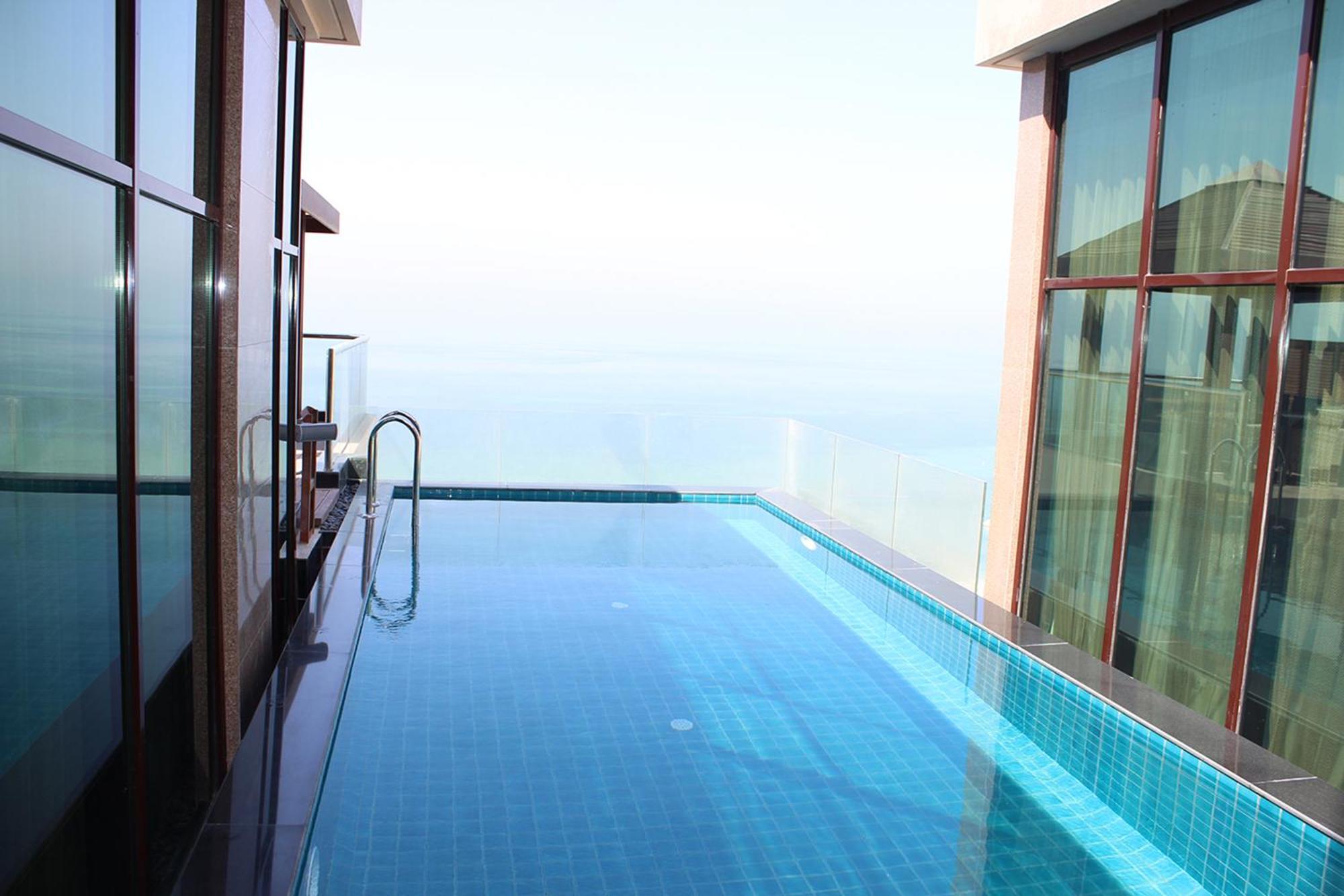 Lagoona Beach Luxury Resort And Spa Manáma Kültér fotó The photo shows an infinity pool situated on a balcony or rooftop, with a clear view extending to the horizon. The pool has a sleek design with blue tiles, and it appears to be reflecting the sky. There is a ladder on one side for access into the poo