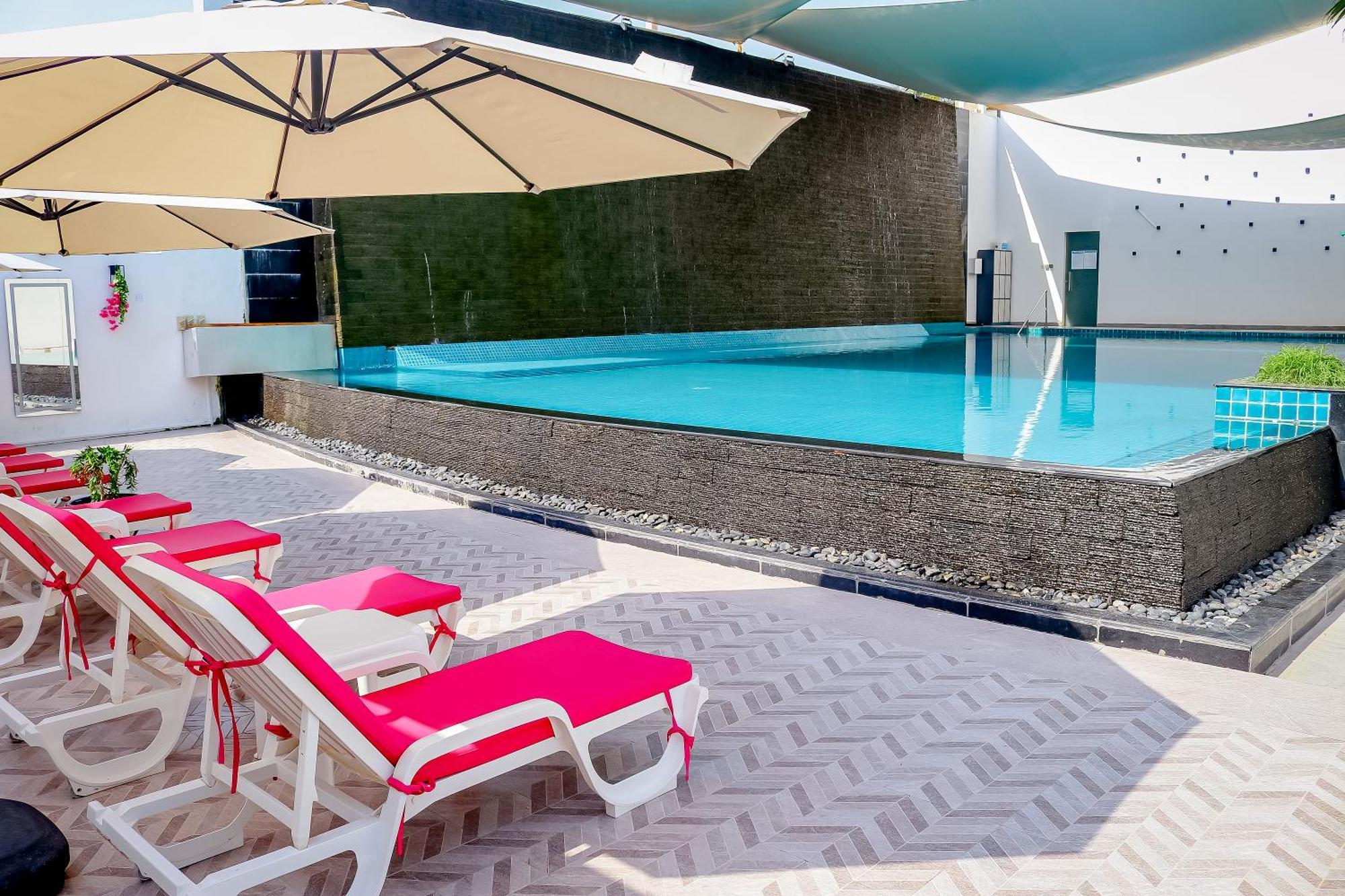 Lagoona Beach Luxury Resort And Spa Manáma Kültér fotó The photo shows a pool area featuring a rectangular swimming pool with clear blue water. Surrounding the pool are light-colored lounge chairs with pink cushions, positioned under large umbrellas for shade. The pool is bordered by a textured wall, and