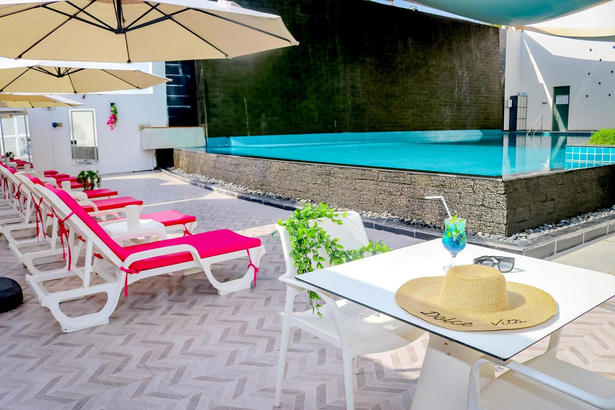 Lagoona Beach Luxury Resort And Spa Manáma Kültér fotó The photo shows a sunny poolside area with bright red lounge chairs arranged neatly beside a swimming pool. There are large beige umbrellas providing shade. A small table is set up with a straw hat and a colorful drink, suggesting a relaxed, tropical