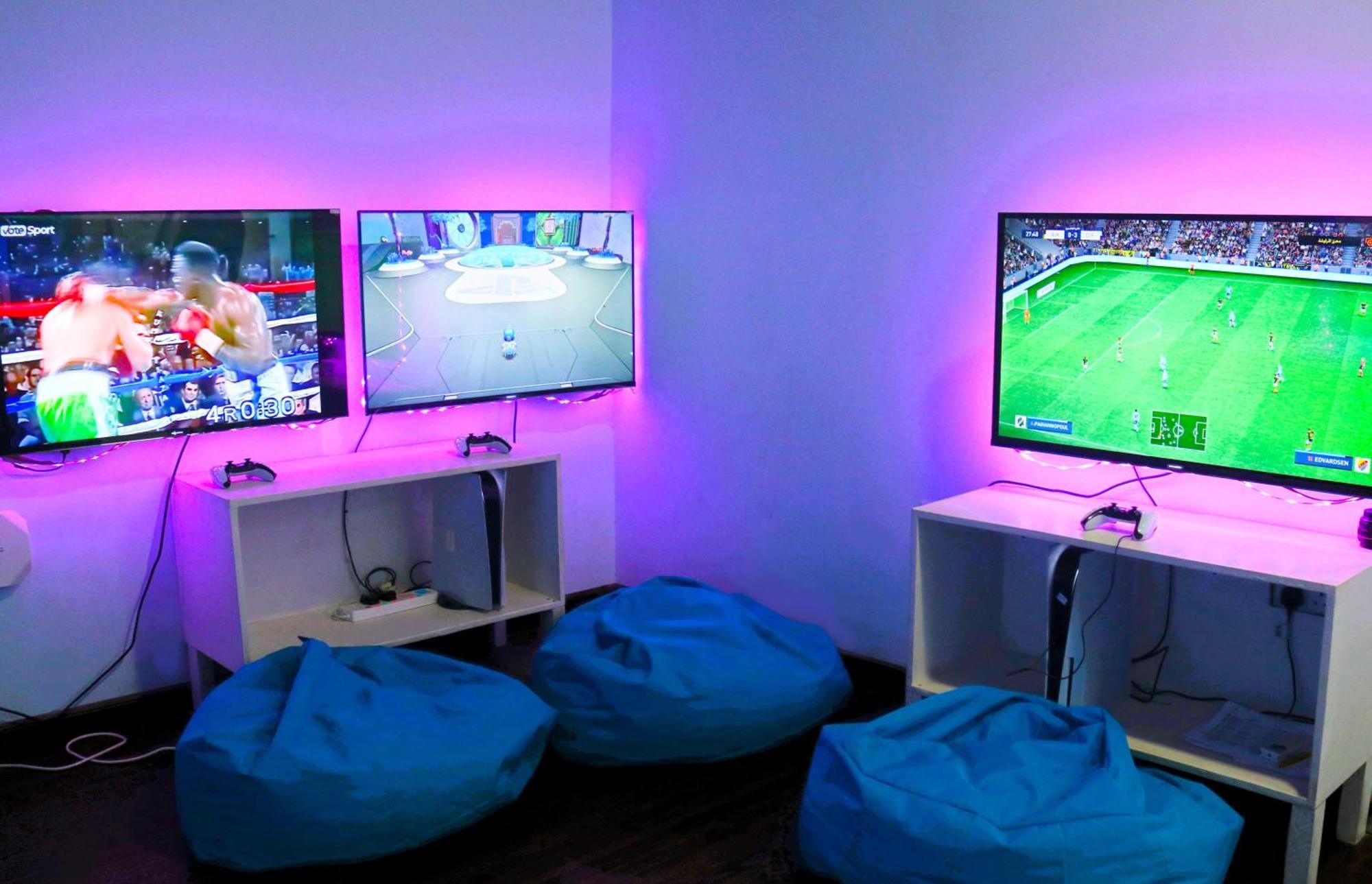 Lagoona Beach Luxury Resort And Spa Manáma Kültér fotó The photo shows a gaming area featuring three televisions mounted on the wall, displaying different games. Two of the TVs are showing gaming scenes, with one depicting a boxing game and the other showing a vibrant game environment. The third TV displ