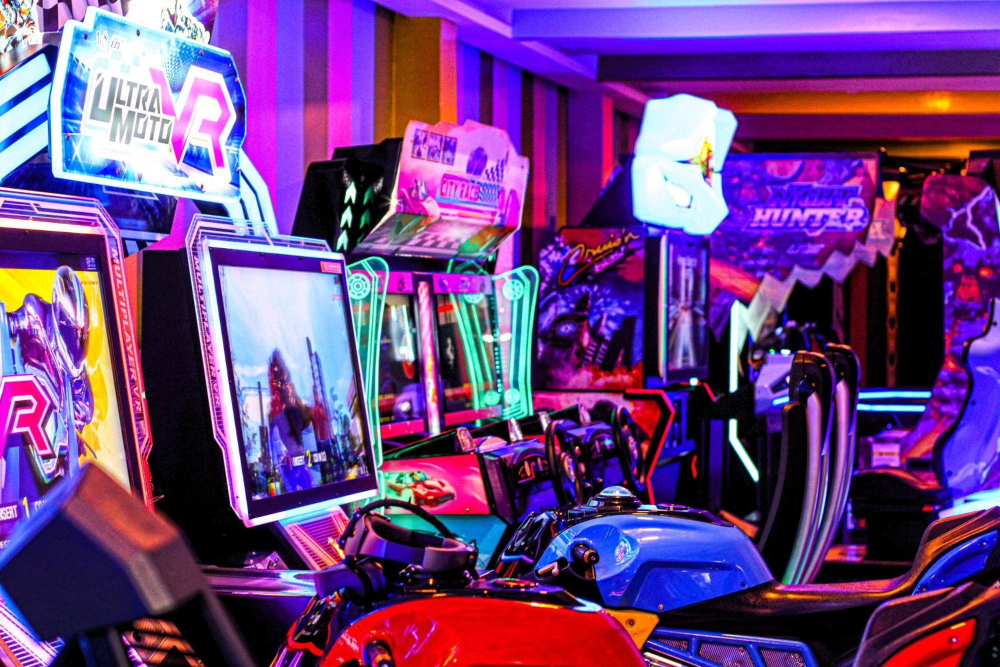 Lagoona Beach Luxury Resort And Spa Manáma Kültér fotó The photo shows a vibrant arcade scene featuring various arcade gaming machines. The machines are lined up, showcasing colorful screens and bright, neon lights, creating an energetic atmosphere. Some machines appear to be racing games, as indicated b