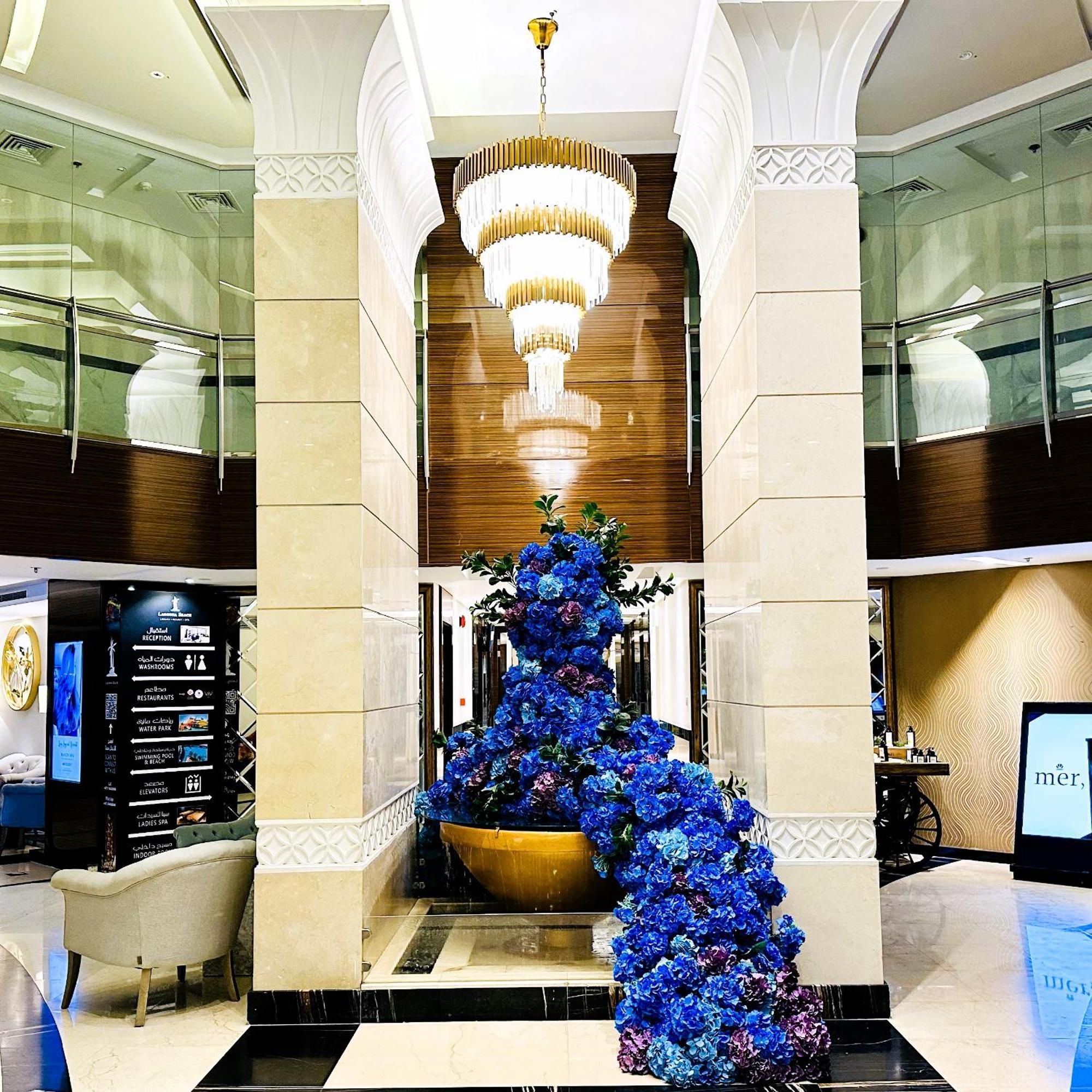Lagoona Beach Luxury Resort And Spa Manáma Kültér fotó The photo depicts an elegant lobby or entrance area of a building. Central to the scene is a large floral arrangement featuring vibrant blue flowers. This arrangement is positioned in a decorative bowl. Above it hangs a stylish chandelier with a laye