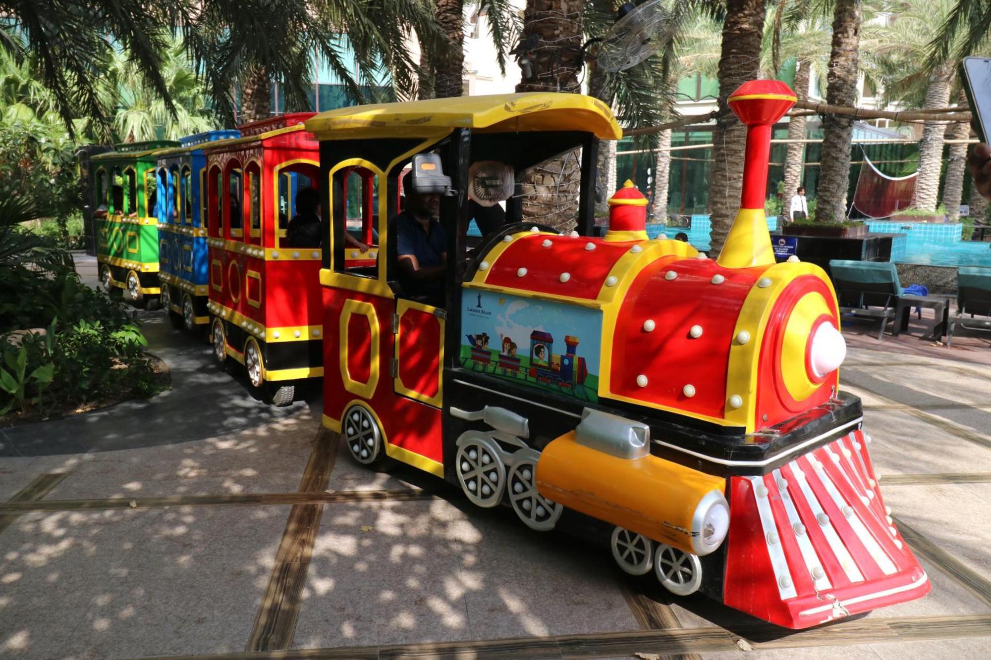 Lagoona Beach Luxury Resort And Spa Manáma Kültér fotó The photo shows a colorful miniature train. It features a vibrant design with bright red, yellow, and blue colors. The front of the train resembles a classic steam engine, complete with a prominent smokestack. The train is designed to resemble a fun 