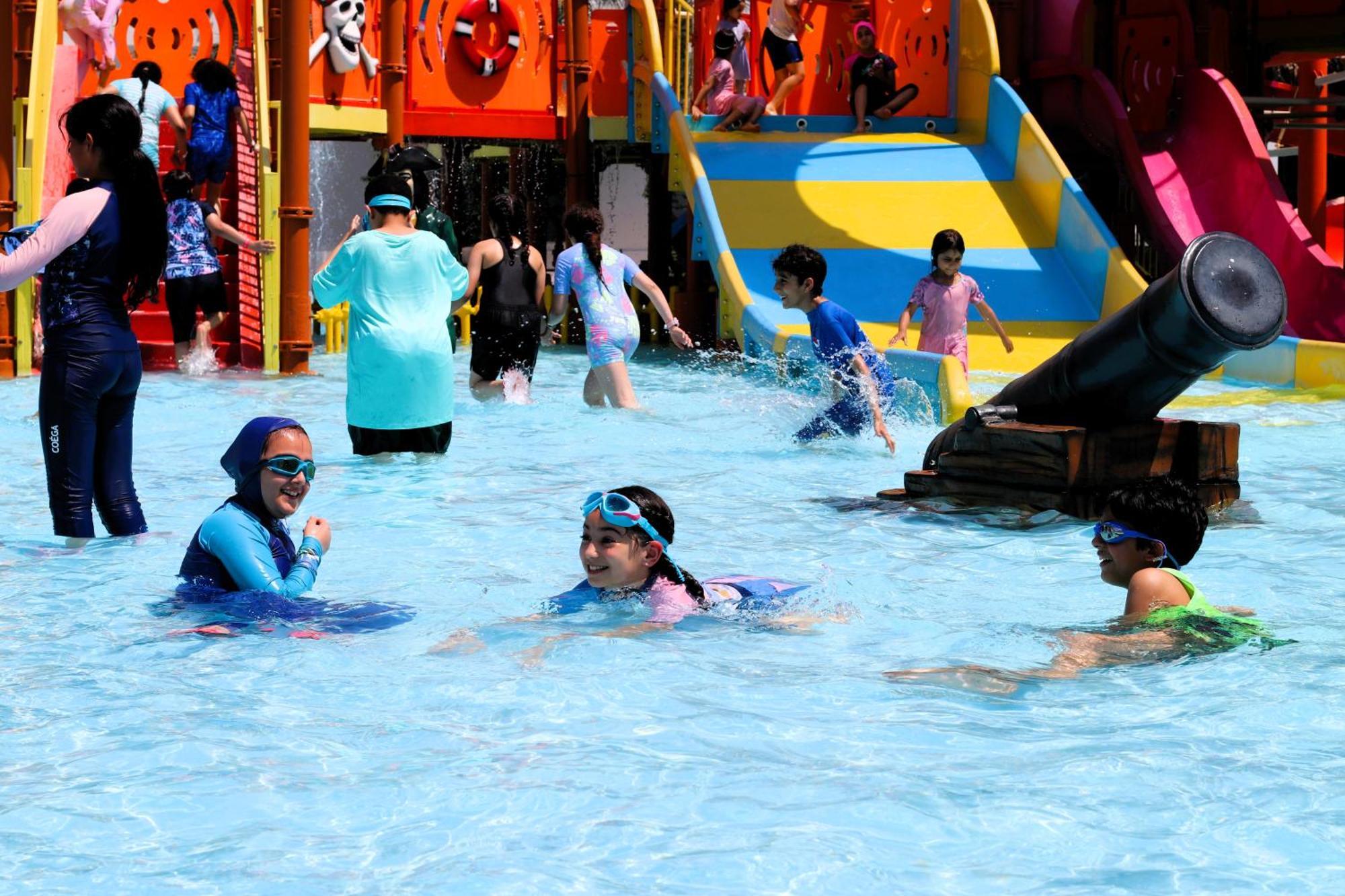 Lagoona Beach Luxury Resort And Spa Manáma Kültér fotó The photo shows a vibrant water park scene with several children playing in a shallow pool. Some are swimming and splashing around, while others are playing on colorful slides in the background. The atmosphere is lively and cheerful, with kids of var