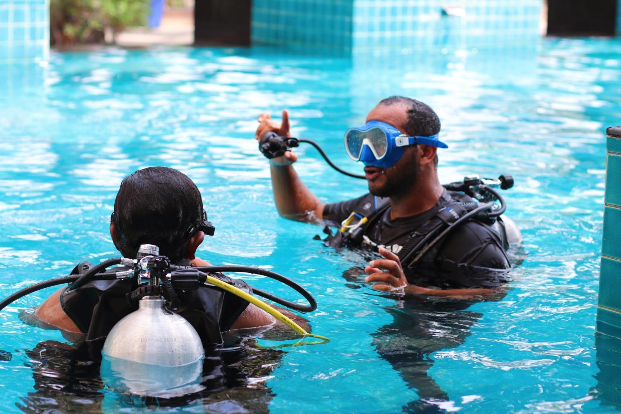 Lagoona Beach Luxury Resort And Spa Manáma Kültér fotó The photo shows two divers in a pool. One diver is wearing a scuba mask and is speaking to the other diver, who is also equipped with scuba gear. They appear to be engaged in a discussion, possibly related to diving instructions or safety. The water 