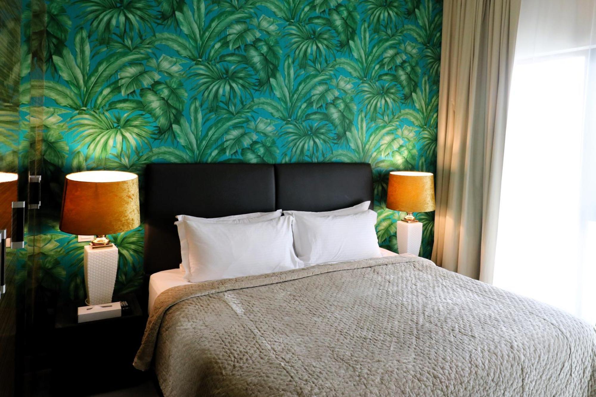 Lagoona Beach Luxury Resort And Spa Manáma Kültér fotó The photo shows a stylish bedroom featuring a large bed with white pillows and a gray blanket. The headboard is upholstered in black, providing a modern touch. Behind the bed, there is a vibrant green wallpaper with a tropical leaf pattern, adding a 