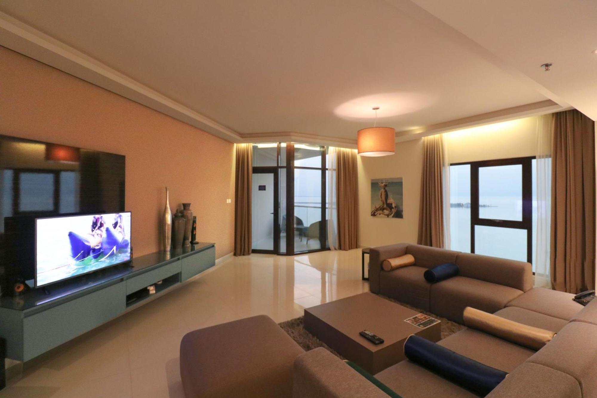Lagoona Beach Luxury Resort And Spa Manáma Kültér fotó The photo shows a modern living room with a sleek design. There is a large wall-mounted television on a contemporary entertainment unit, with decorative items placed beside it. The room features a comfortable sectional sofa in light tones, with a cof
