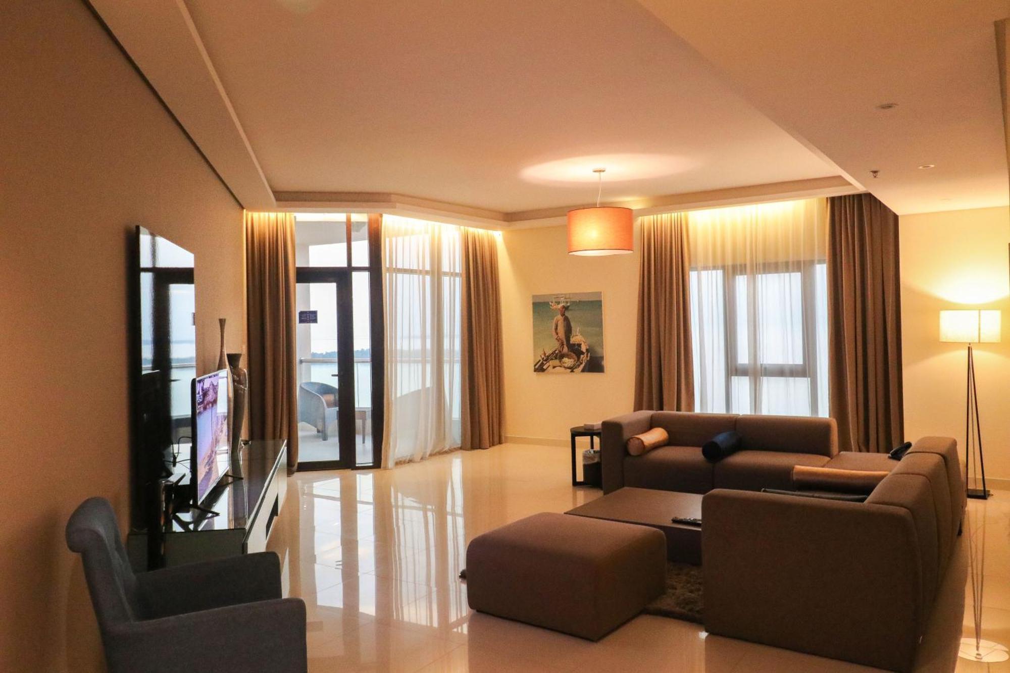 Lagoona Beach Luxury Resort And Spa Manáma Kültér fotó The photo shows a modern living room with a spacious and elegant design. It features a large couch in neutral tones, a soft ottoman, and a stylish coffee table. The walls are painted in a light color, and there are large windows with sheer curtains a