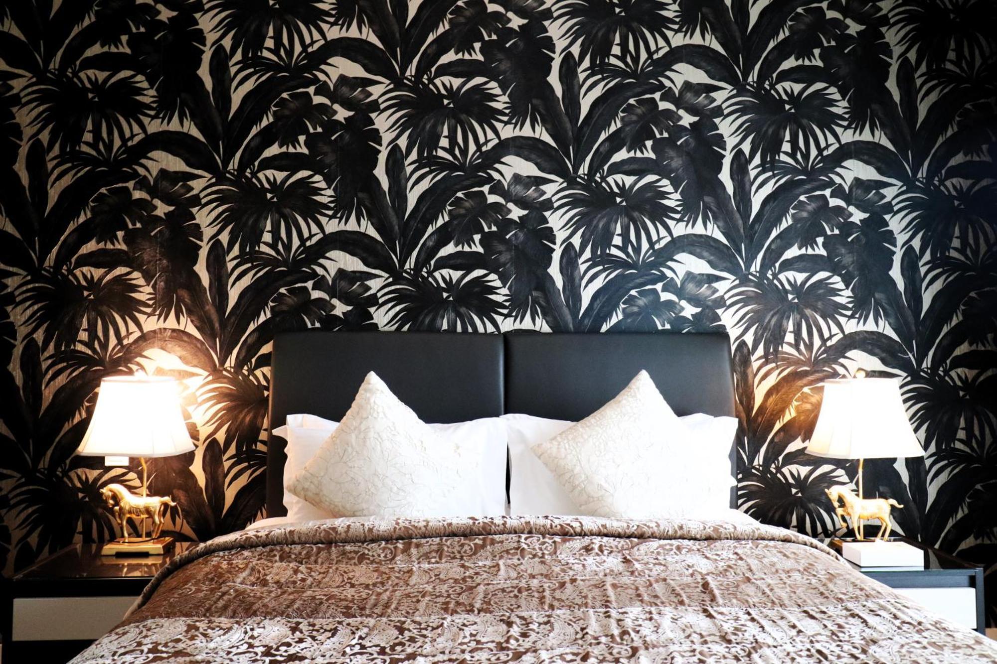 Lagoona Beach Luxury Resort And Spa Manáma Kültér fotó The photo depicts a stylish bedroom featuring a distinctive wall covered in a black and white tropical foliage wallpaper. The bed has a modern black headboard and is adorned with white pillows, creating a clean and elegant look. A textured brown thro