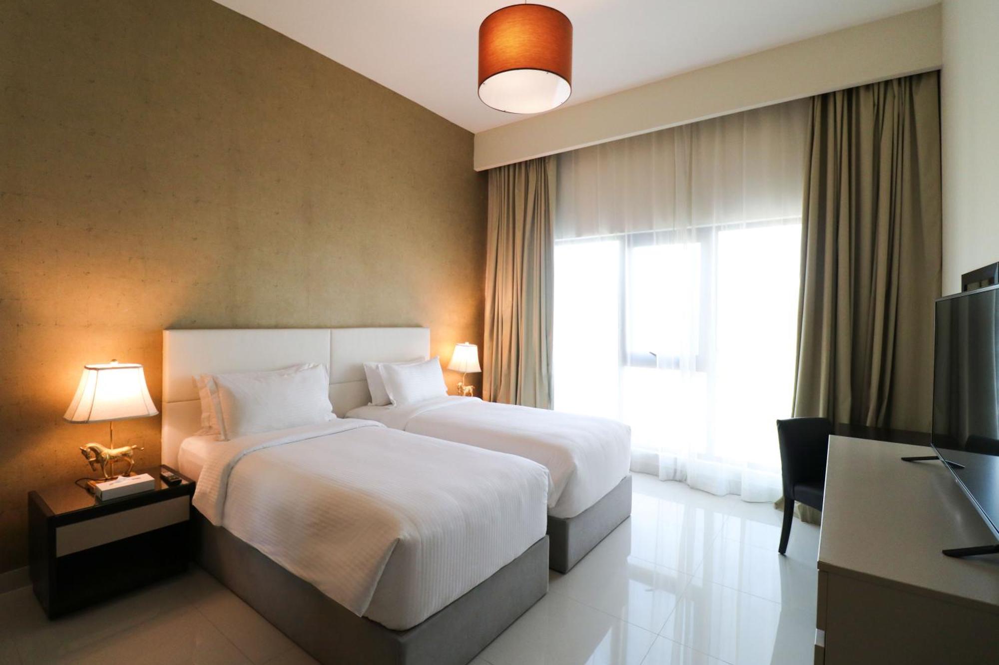 Lagoona Beach Luxury Resort And Spa Manáma Kültér fotó The photo shows a hotel room featuring two single beds with white bedding. The walls have a neutral tone, and there's a large window covered by light, sheer curtains allowing natural light to enter. On either side of the beds, there are bedside table